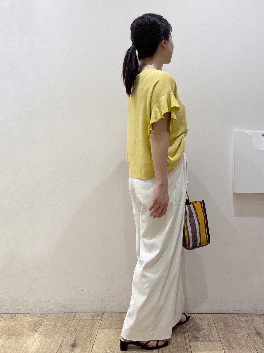 イエロー系のニット/セーター、ホワイト系のその他パンツ、ブラウン系のトートバッグを着用したレディースの春コーディネートの4枚目の写真