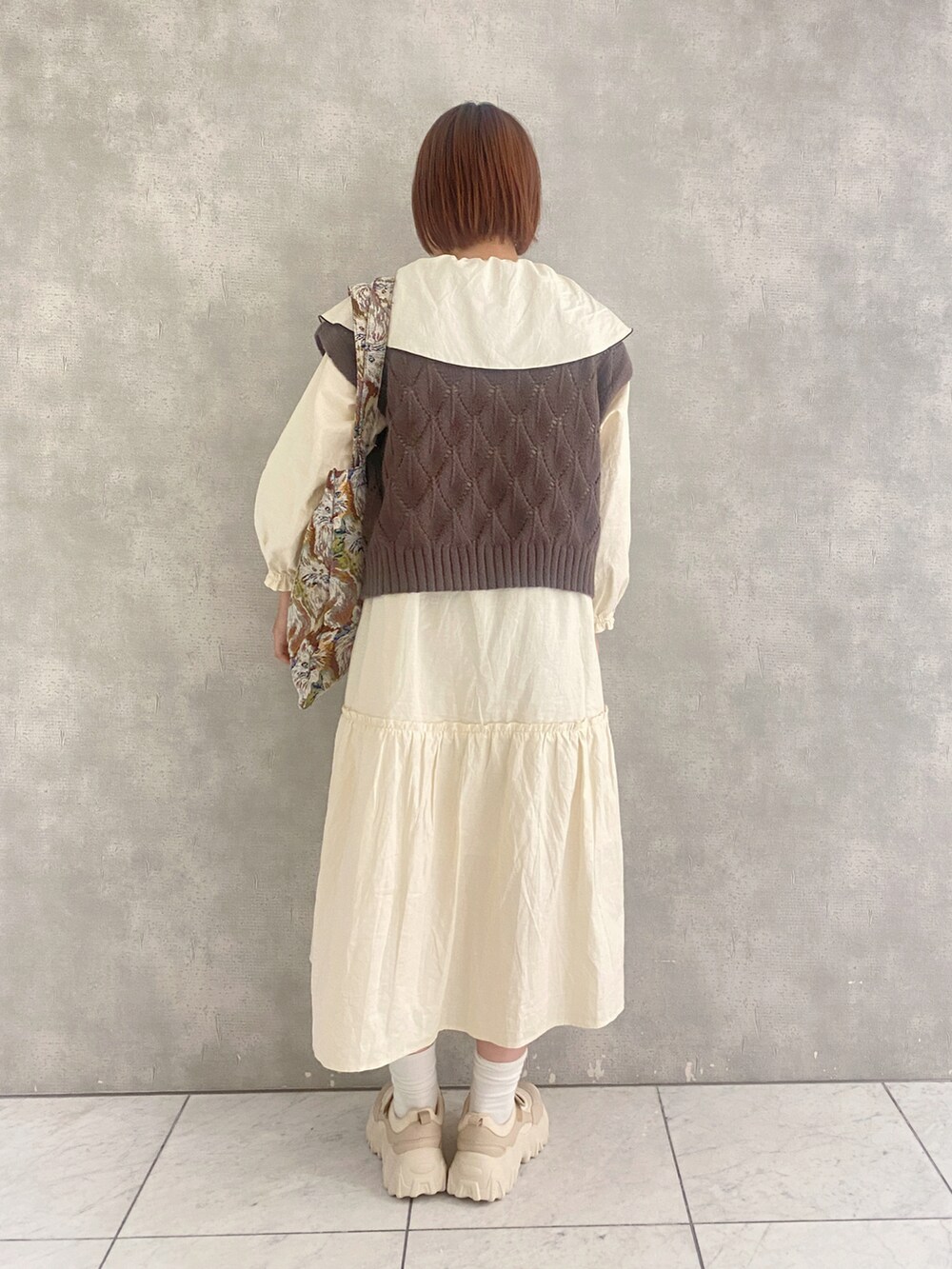 ベージュ系のスニーカー、ホワイト系のワンピース、ブラウン系のベストを着用したレディースの秋コーディネートの2枚目の写真
