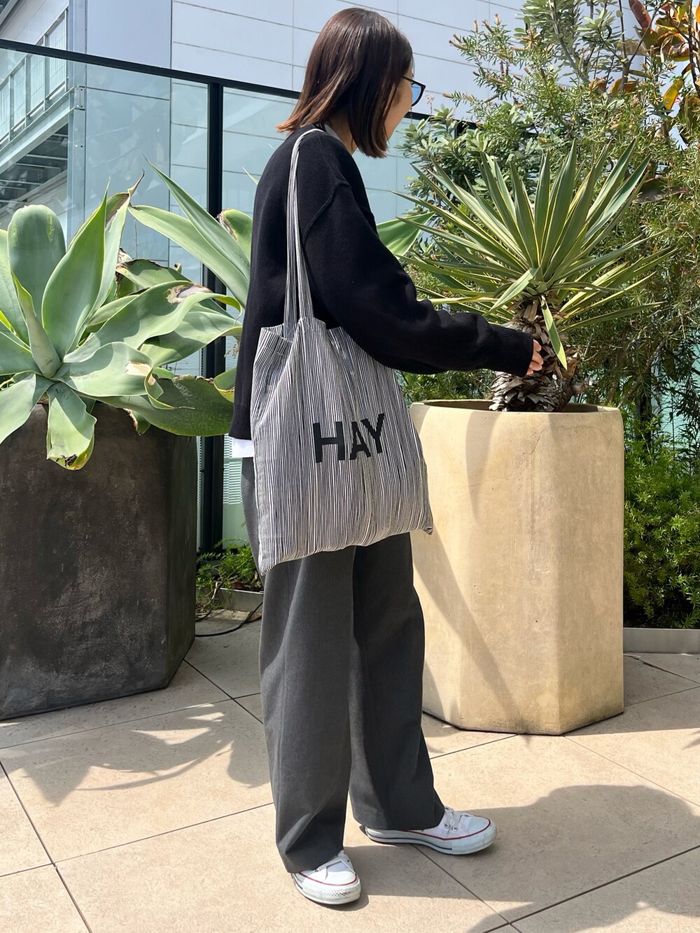 ブラック系のニット/セーター、ホワイト系のTシャツ/カットソー、グレー系のスラックスを着用したレディースの春コーディネートの2枚目の写真