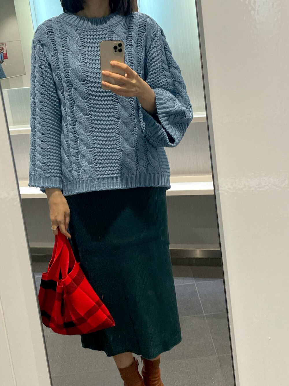 レッド系のハンドバッグ、ブルー系のニット/セーターを着用したレディースの冬コーディネートの2枚目の写真