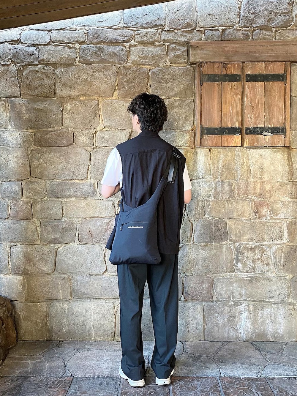 ブラック系のベスト、ホワイト系のTシャツ/カットソー、ブラック系のスラックスを着用したメンズの夏コーディネートの2枚目の写真