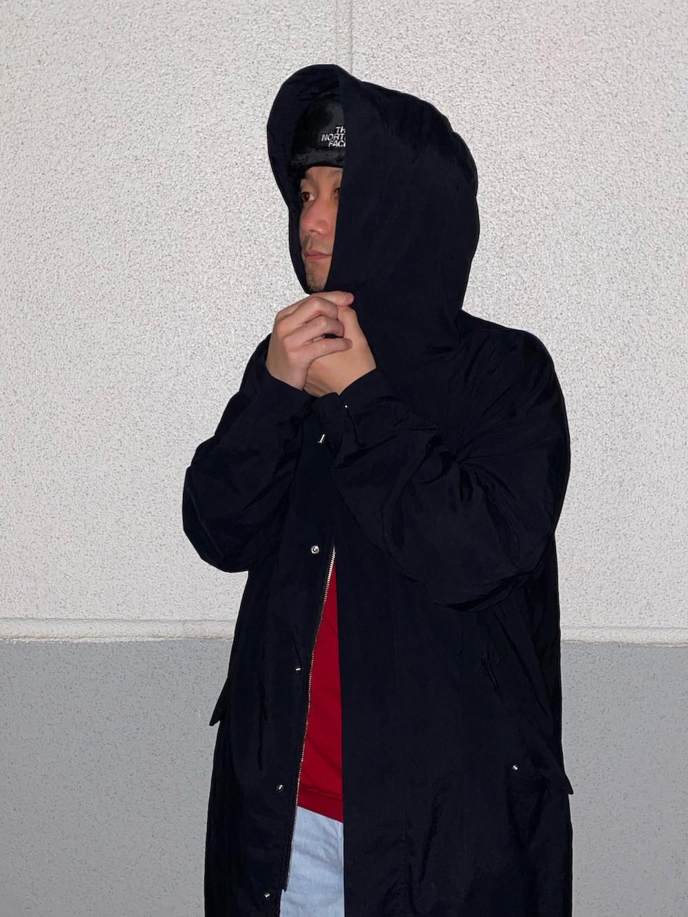 レッド系のニット/セーター、ブラック系のその他アウター、ブルー系のデニムパンツを着用したメンズの春コーディネートの2枚目の写真