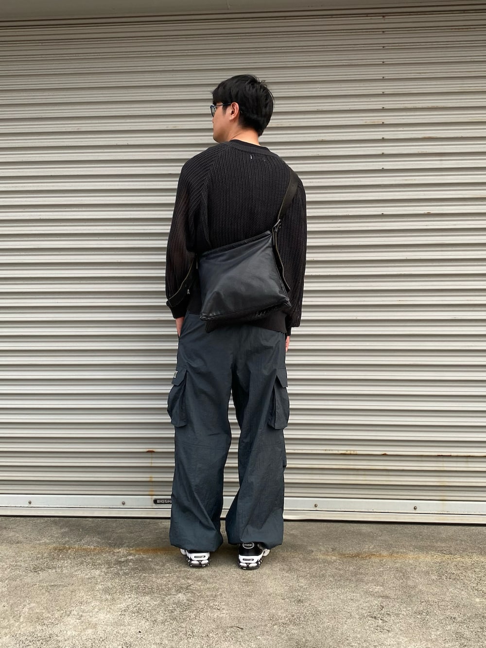 ブラック系のニット/セーター、ブラック系のショルダーバッグ、ブルー系のカーゴパンツを着用したメンズの秋コーディネートの2枚目の写真