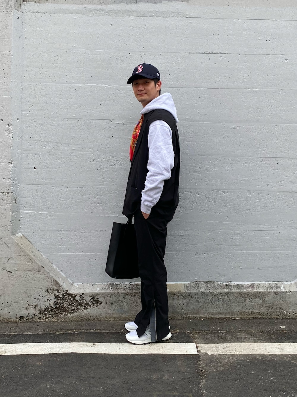 ブラック系のベスト、グレー系のパーカー、ブラック系のバッグを着用したメンズの春コーディネートの2枚目の写真