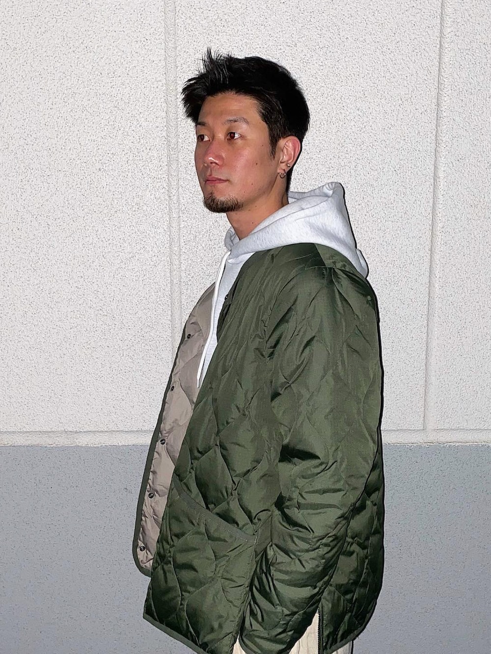 グリーン系のミリタリージャケット、グレー系のパーカー、ホワイト系のパンツを着用したメンズの冬コーディネートの2枚目の写真