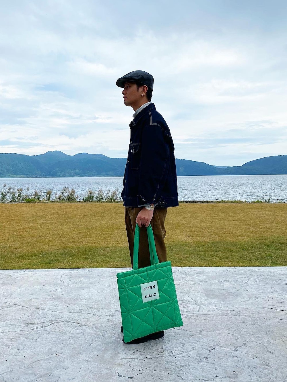 ブラック系のデニムジャケット、グリーン系のトートバッグ、ブラック系のドレスシューズを着用したメンズの冬コーディネートの2枚目の写真