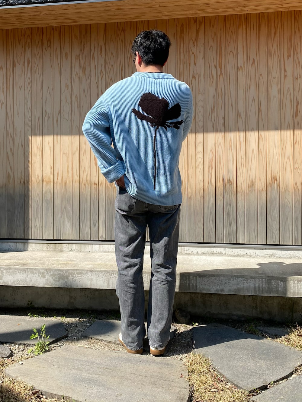 ブルー系のニット/セーター、ブラック系のデニムパンツ、ホワイト系のスニーカーを着用したメンズの春コーディネートの2枚目の写真