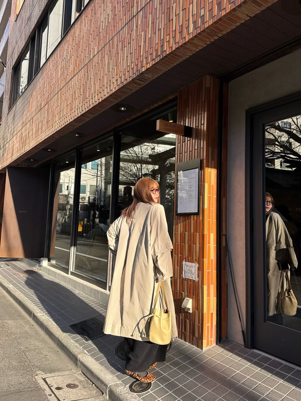 ベージュ系のショルダーバッグ、ベージュ系のステンカラーコート、ブラック系のワンピースを着用したレディースの冬コーディネートの2枚目の写真