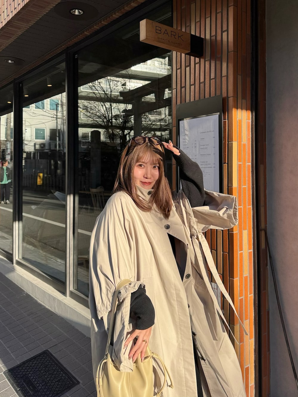 ベージュ系のショルダーバッグ、ベージュ系のステンカラーコート、ブラック系のワンピースを着用したレディースの冬コーディネートの3枚目の写真