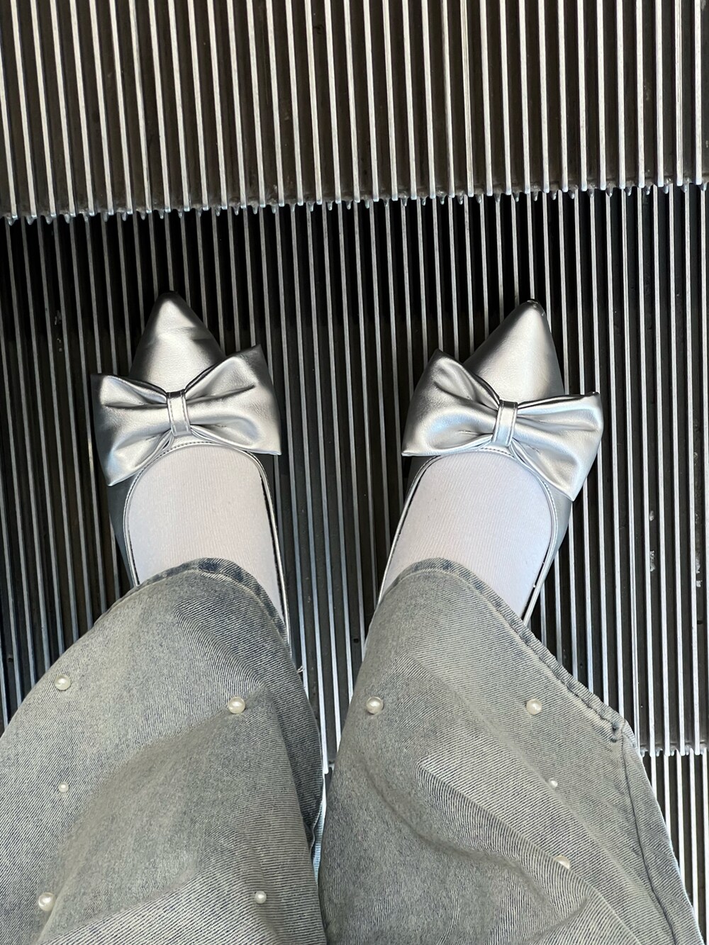 シルバー系のトートバッグ、シルバー系のパンプス、ブルー系のデニムパンツを着用したレディースの冬コーディネートの4枚目の写真