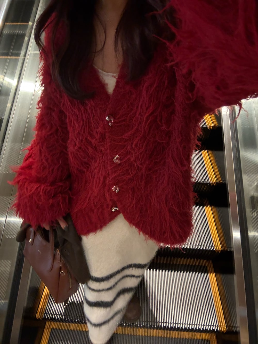 ブラウン系のボストンバッグ、レッド系のニット/セーター、ホワイト系のスカートを着用したレディースの冬コーディネートの3枚目の写真