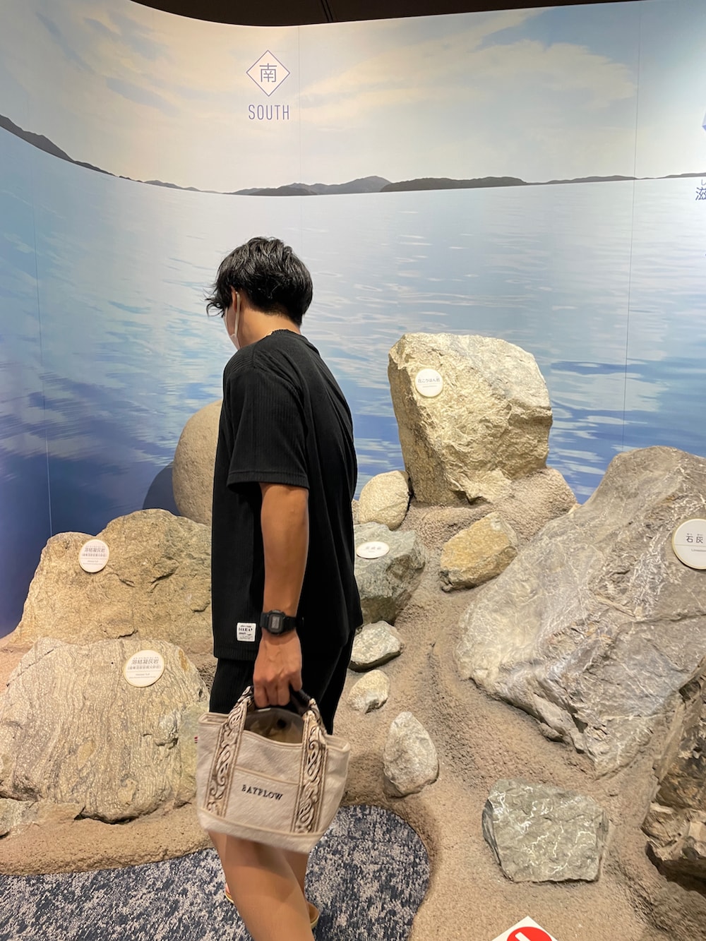 ベージュ系のトートバッグ、ブラック系のルームウェア、ゴールド系のネックレスを着用したメンズの夏コーディネートの2枚目の写真