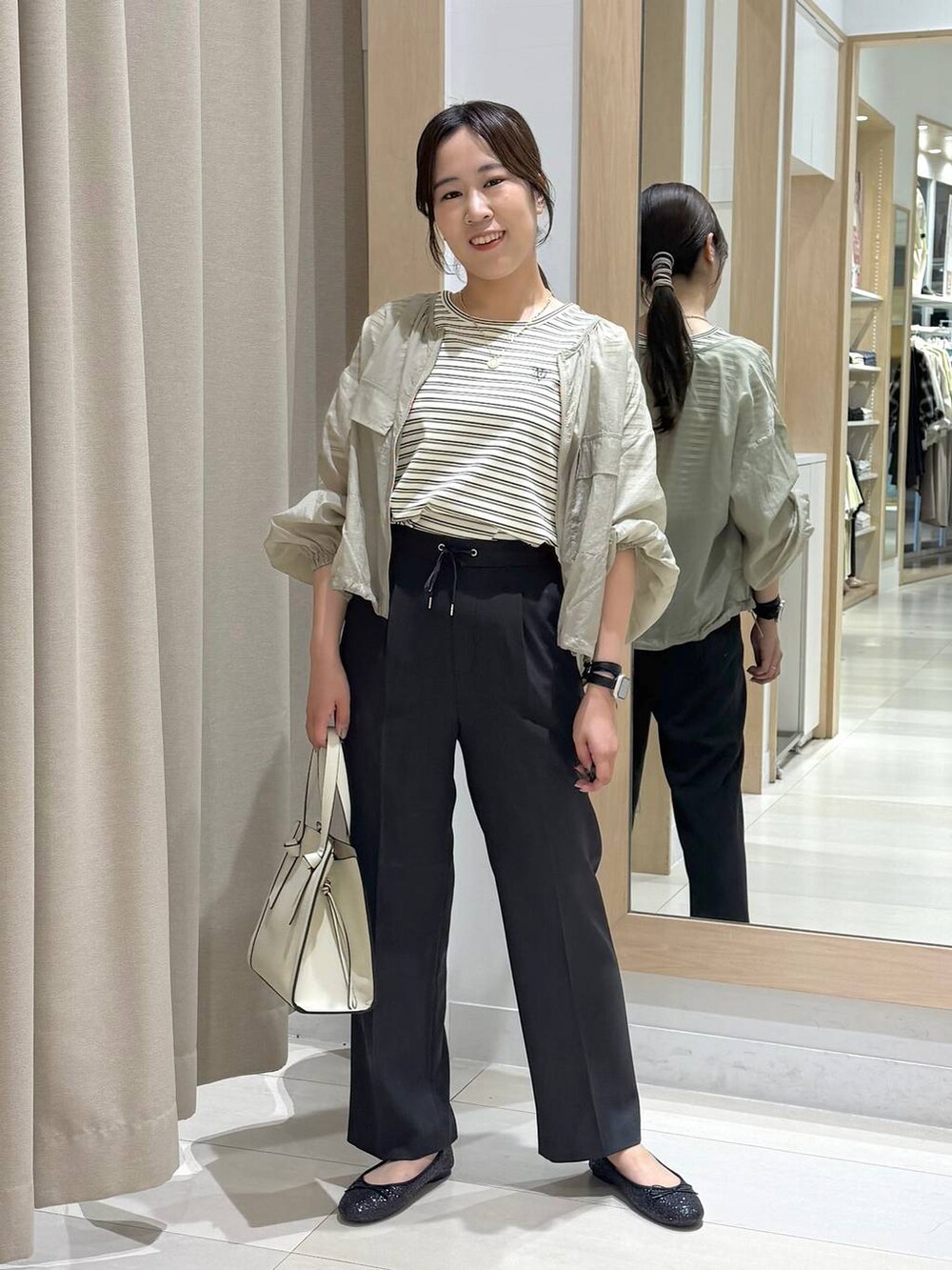 ブラック系のバレエシューズ、ホワイト系のショルダーバッグ、グリーン系のブルゾンを着用したレディースの春コーディネートの2枚目の写真