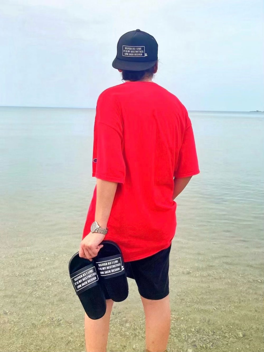 レッド系のTシャツ/カットソー、ブラック系のサンダル、ブラック系のキャップを着用したメンズの春コーディネートの4枚目の写真