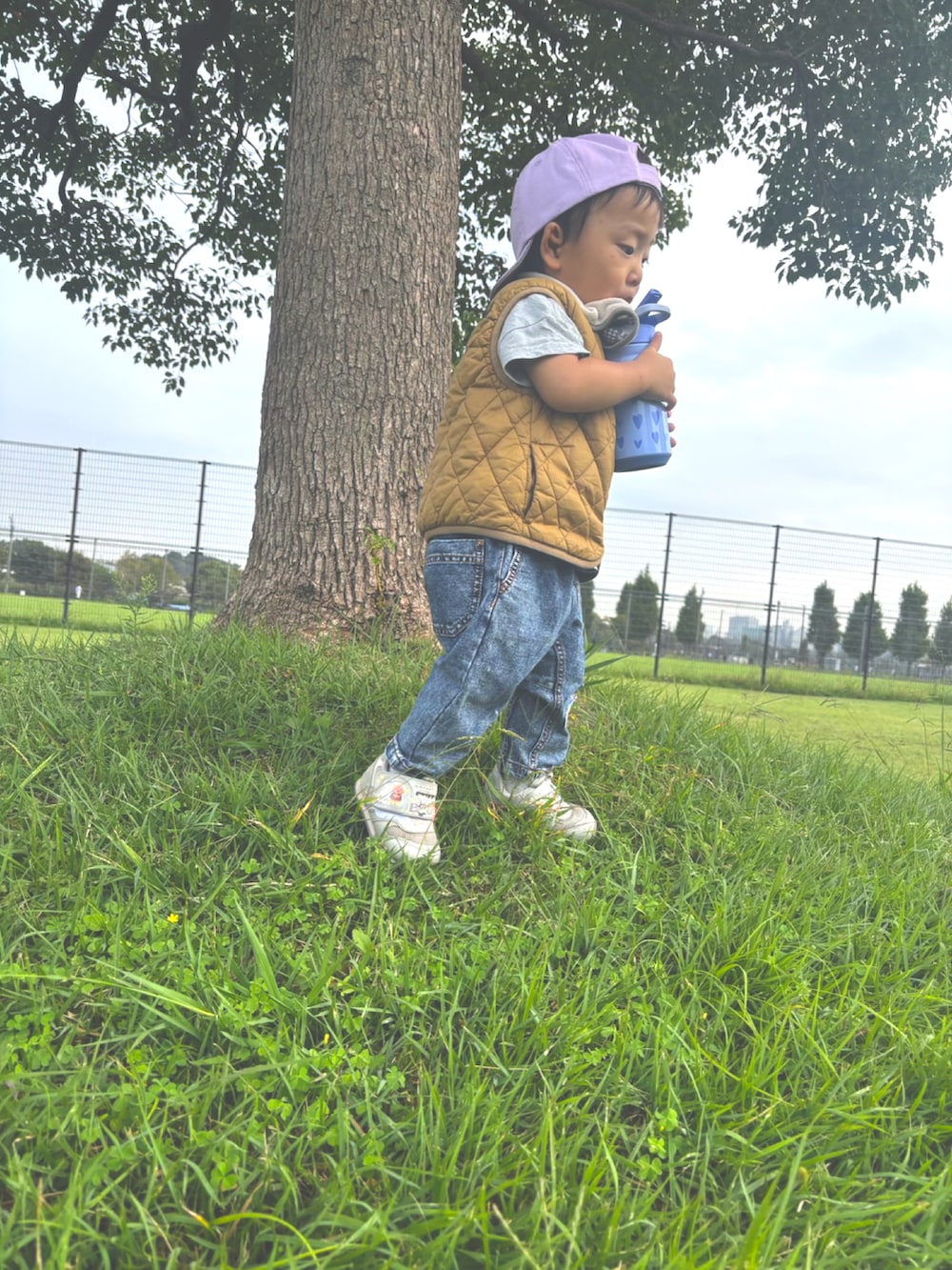 ベージュ系のベスト、グレー系のスニーカー、パープル系のキャップを着用したキッズの秋コーディネートの2枚目の写真