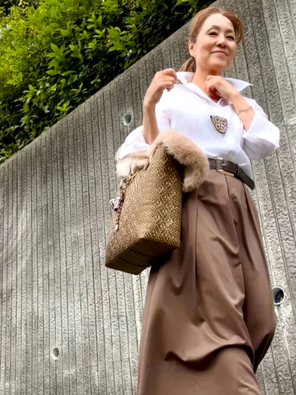 ゴールド系のかごバッグ、ブラウン系のスカート、ホワイト系のスニーカーを着用したレディースの秋コーディネートの2枚目の写真