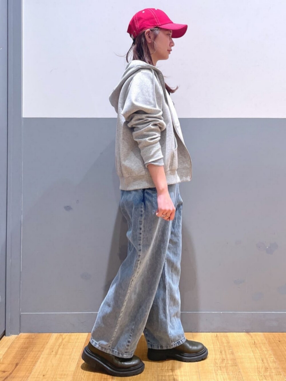 グレー系のパーカー、ブルー系のサロペット/オーバーオール、レッド系のキャップを着用したレディースの春コーディネートの2枚目の写真