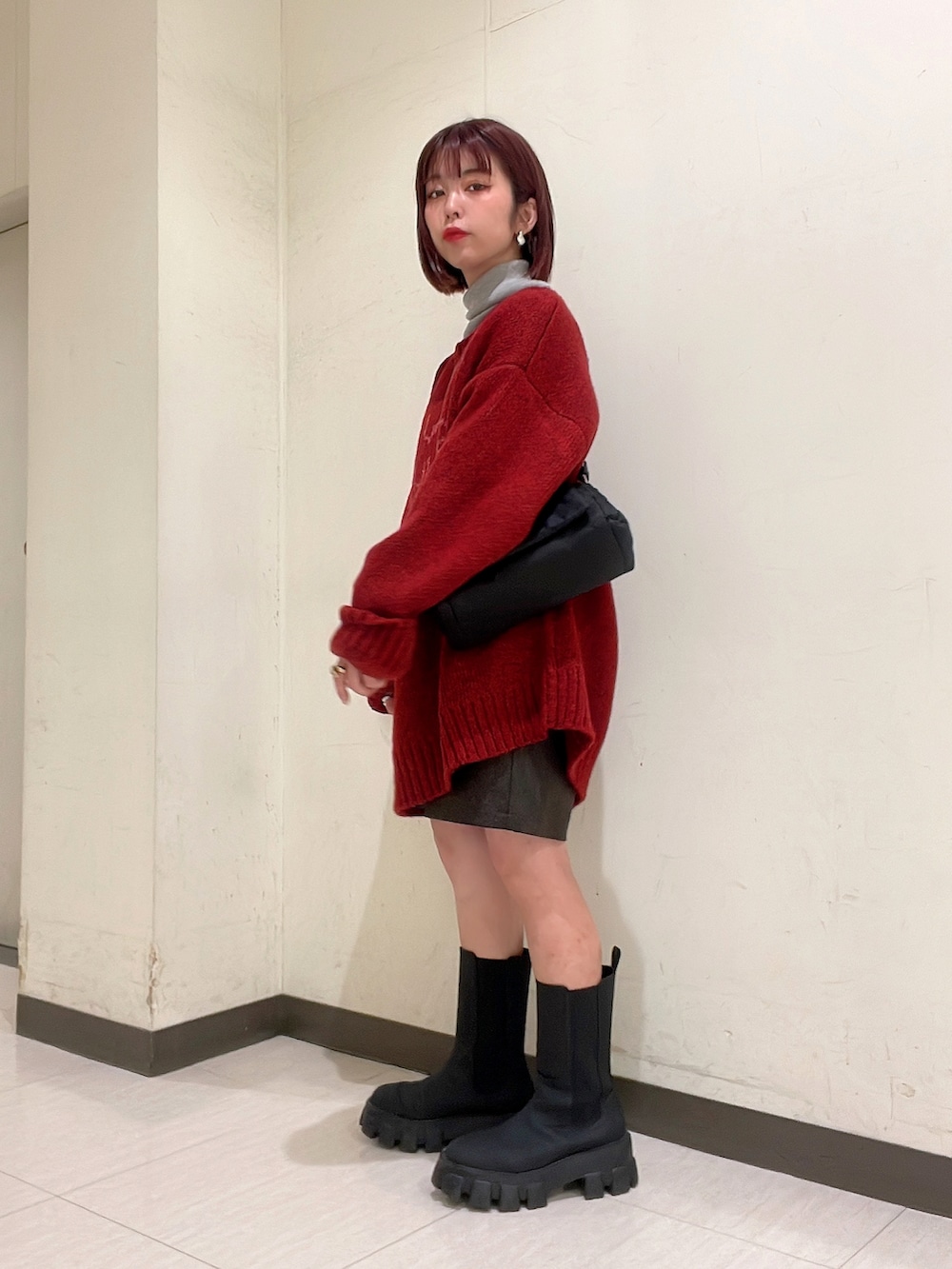 レッド系のニット/セーター、ブラック系のブーツ、ブラック系のショルダーバッグを着用したレディースの冬コーディネートの3枚目の写真