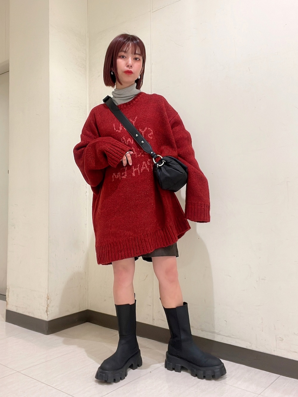 レッド系のニット/セーター、ブラック系のブーツ、ブラック系のショルダーバッグを着用したレディースの冬コーディネートの2枚目の写真