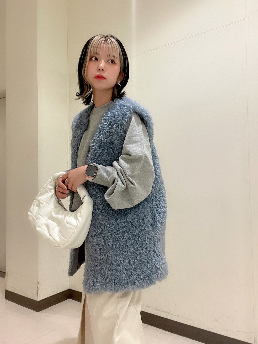 ホワイト系のショルダーバッグ、ブルー系のベスト、グレー系のスウェットを着用したレディースの秋コーディネートの4枚目の写真