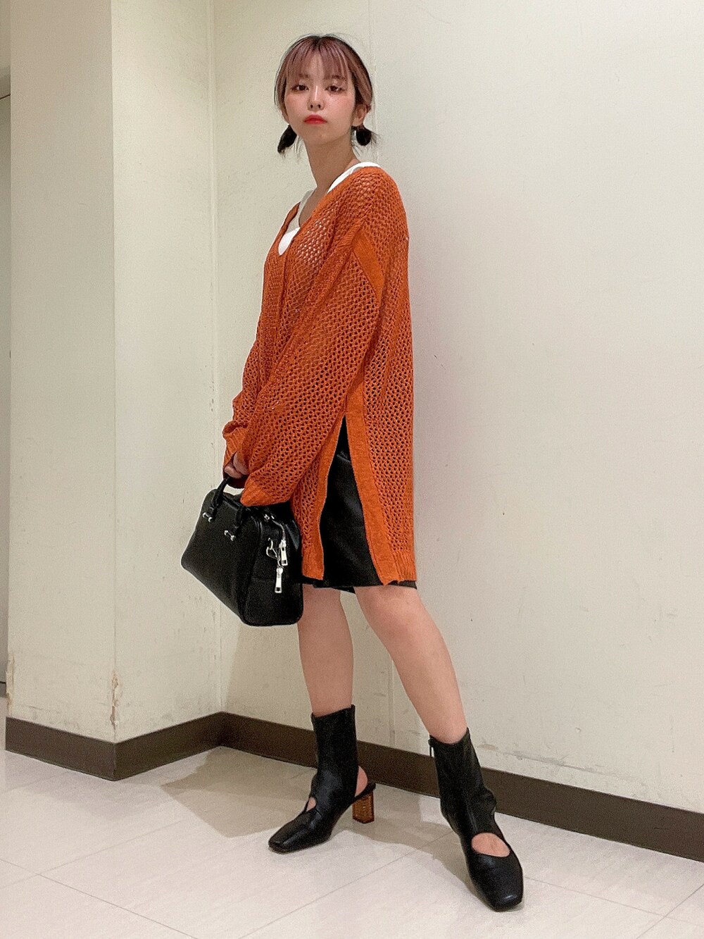 ブラック系のボストンバッグ、ブラック系のブーツ、オレンジ系のニット/セーターを着用したレディースの夏コーディネートの3枚目の写真