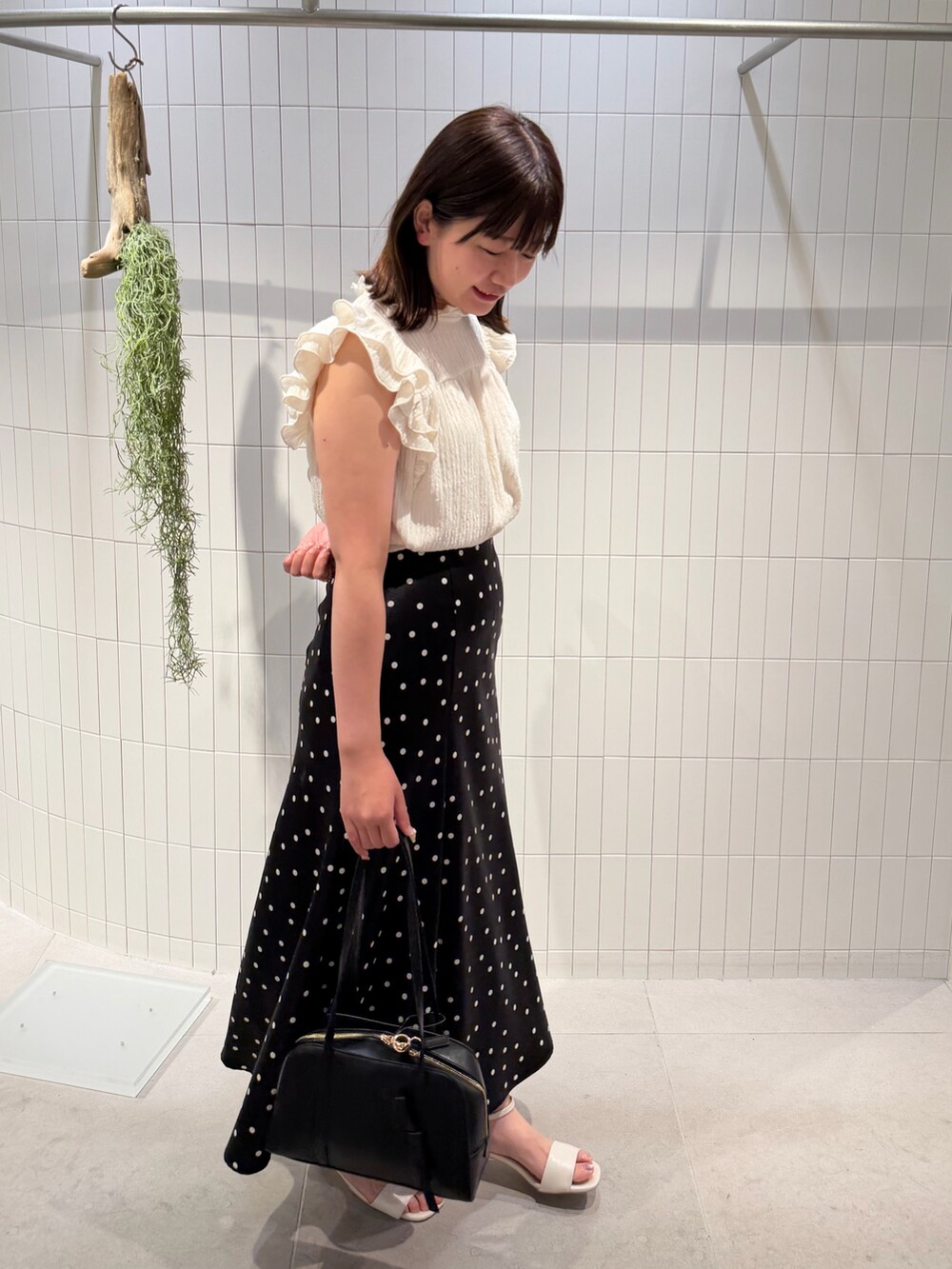ブラック系のスカート、ホワイト系のTシャツ/カットソー、ブラック系のボストンバッグを着用したレディースの夏コーディネートの2枚目の写真