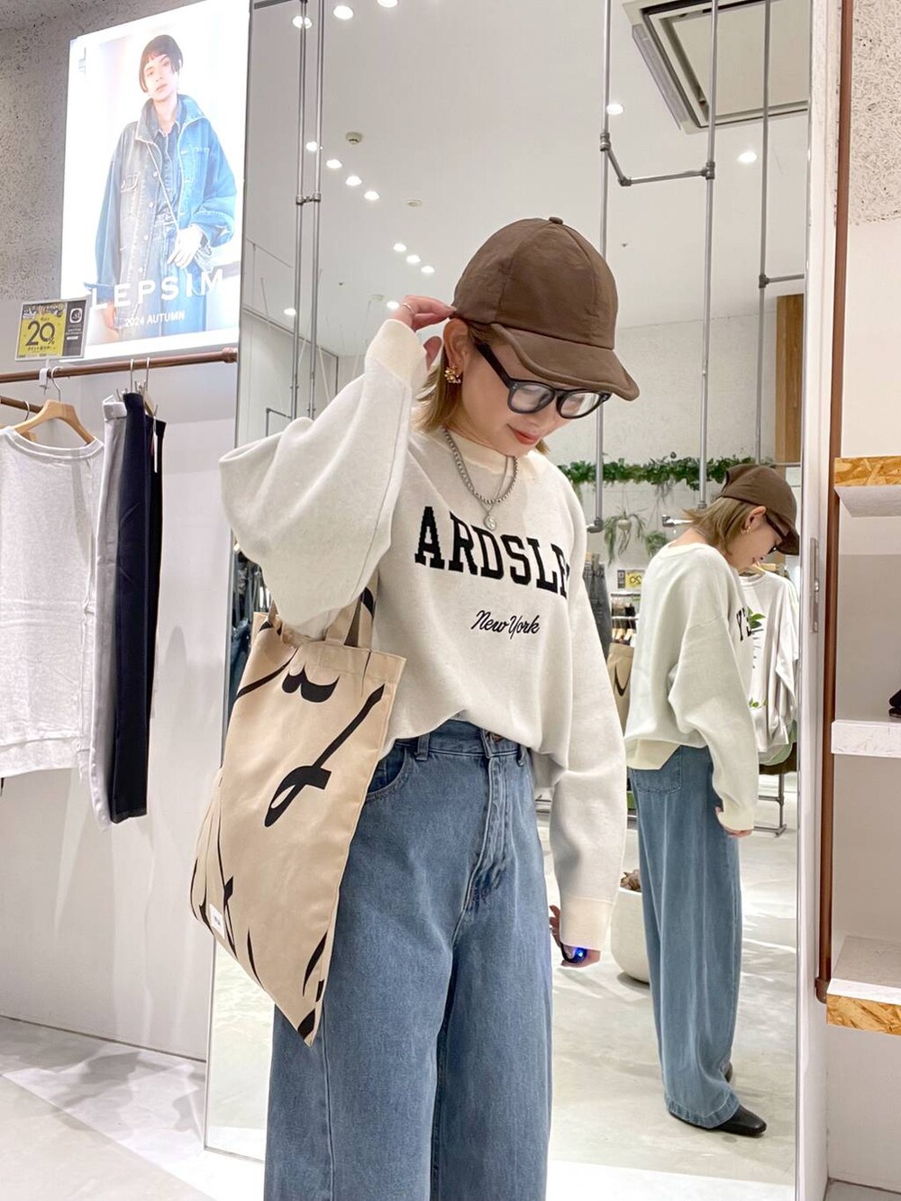 ブラウン系のトートバッグ、ブルー系のデニムパンツ、ホワイト系のニット/セーターを着用したレディースの秋コーディネートの4枚目の写真