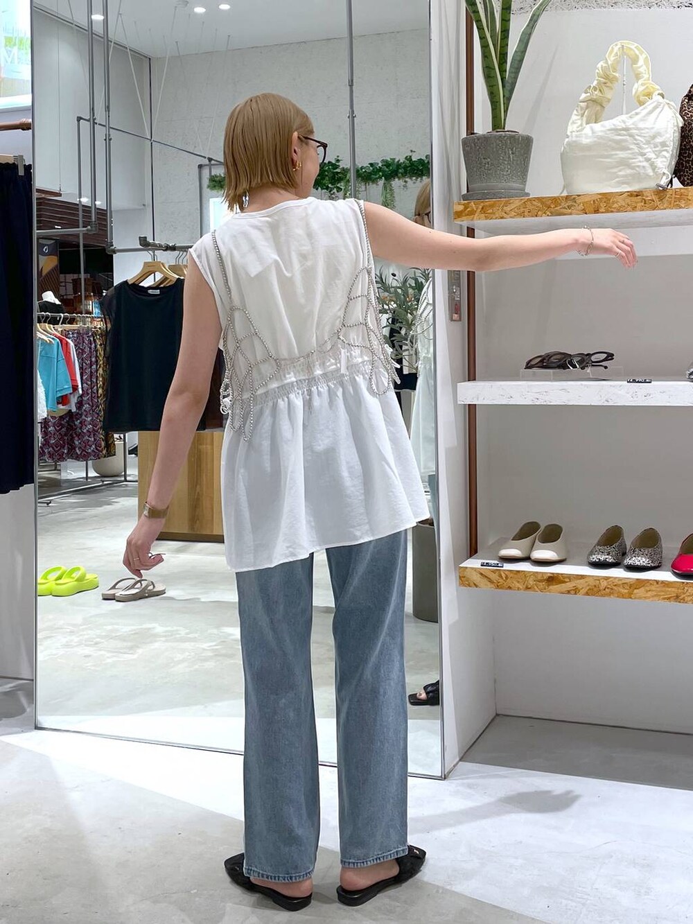 シルバー系のベスト、ホワイト系のタンクトップ、ブルー系のデニムパンツを着用したレディースの夏コーディネートの3枚目の写真