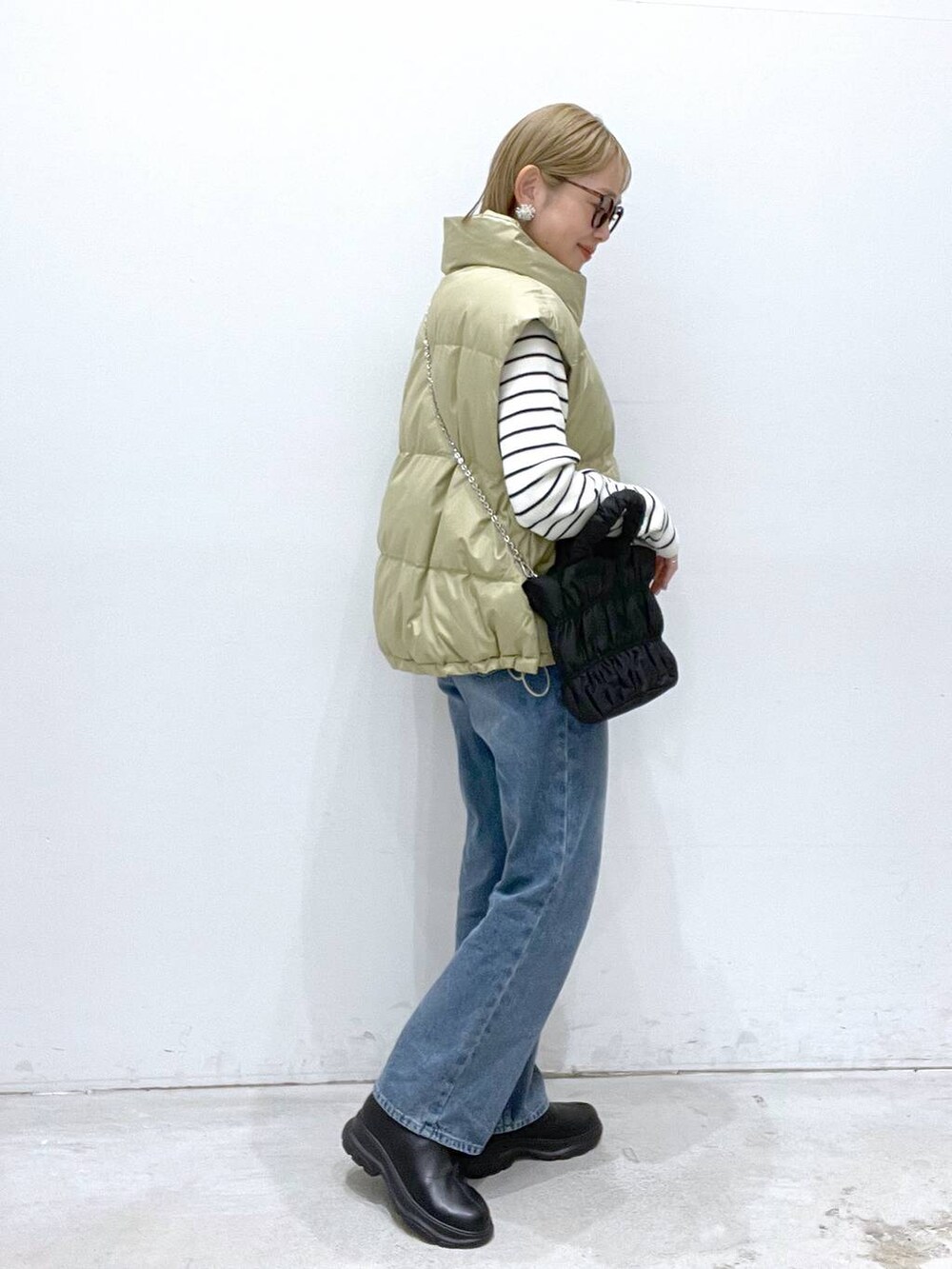ベージュ系のダウンベスト、ブルー系のデニムパンツ、ブラック系のブーツを着用したレディースの冬コーディネートの2枚目の写真