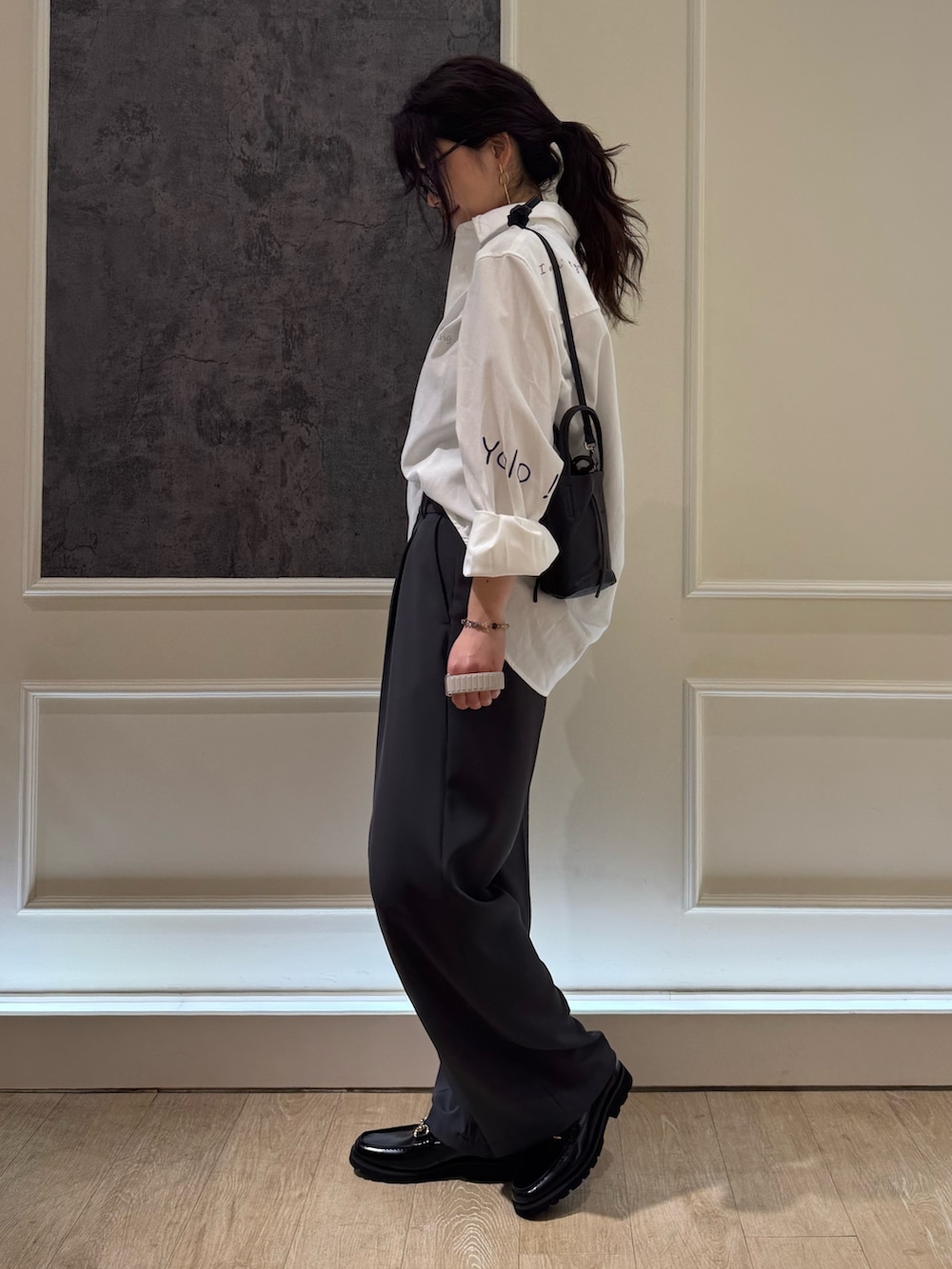 ホワイト系のシャツ/ブラウス、グレー系のスラックス、ブラック系のショルダーバッグを着用したレディースの春コーディネートの2枚目の写真