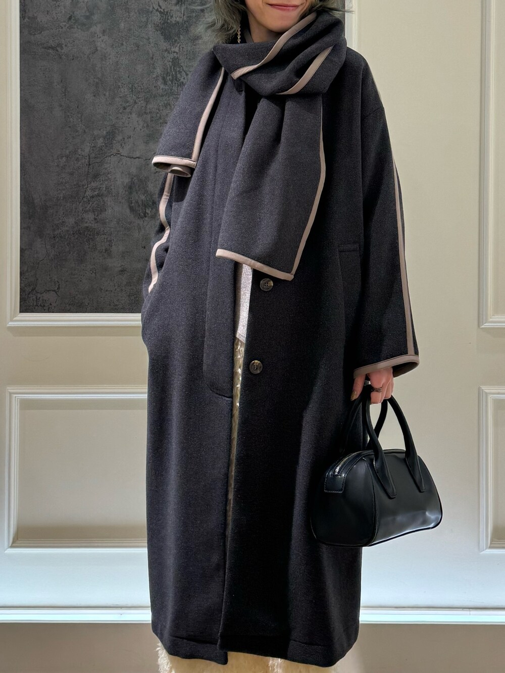 グレー系のノーカラーコート、ホワイト系のスカート、ベージュ系のニット/セーターを着用したレディースの冬コーディネートの2枚目の写真