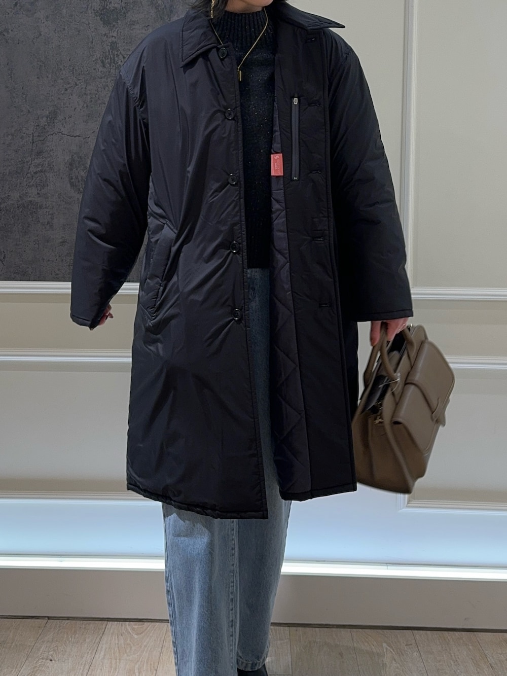 ブラック系のステンカラーコート、ブルー系のデニムパンツ、ブラック系のブーツを着用したレディースの冬コーディネートの2枚目の写真