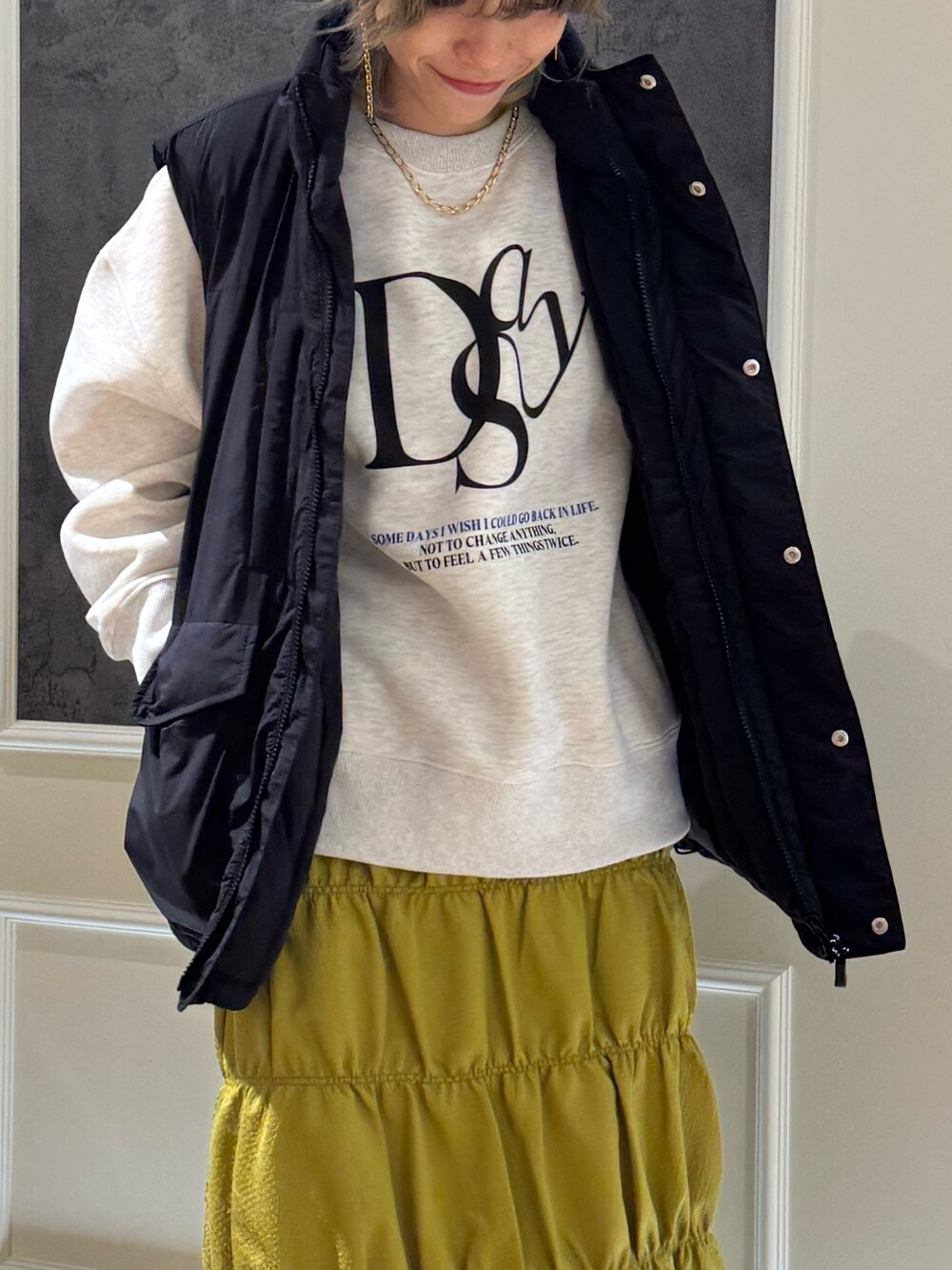 ブラック系のベスト、グレー系のスウェット、イエロー系のスカートを着用したレディースの秋コーディネートの2枚目の写真