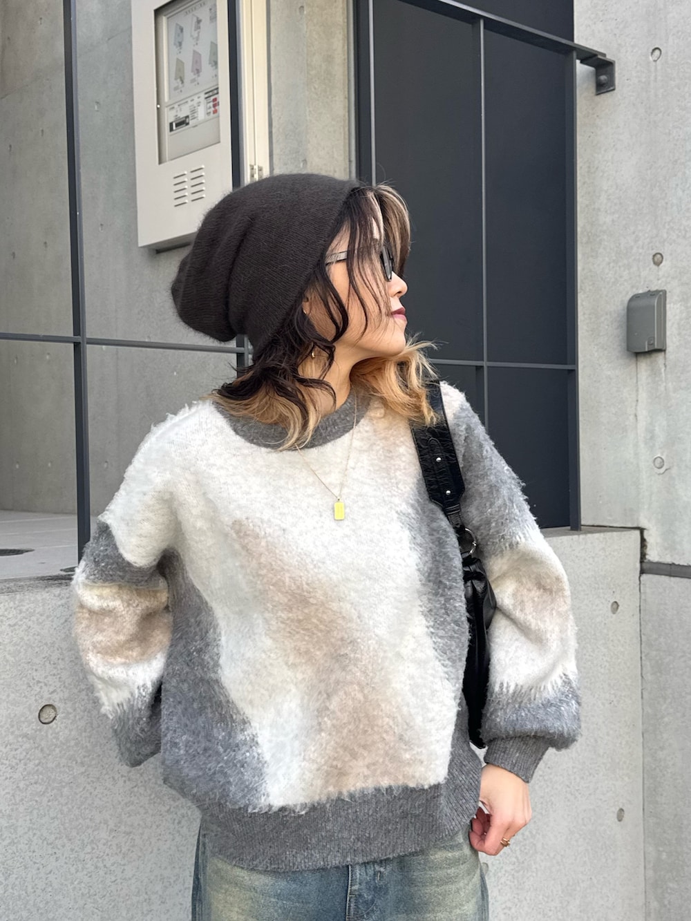 グレー系のニット/セーター、ブルー系のデニムパンツ、ブラック系のショルダーバッグを着用したレディースの冬コーディネートの2枚目の写真