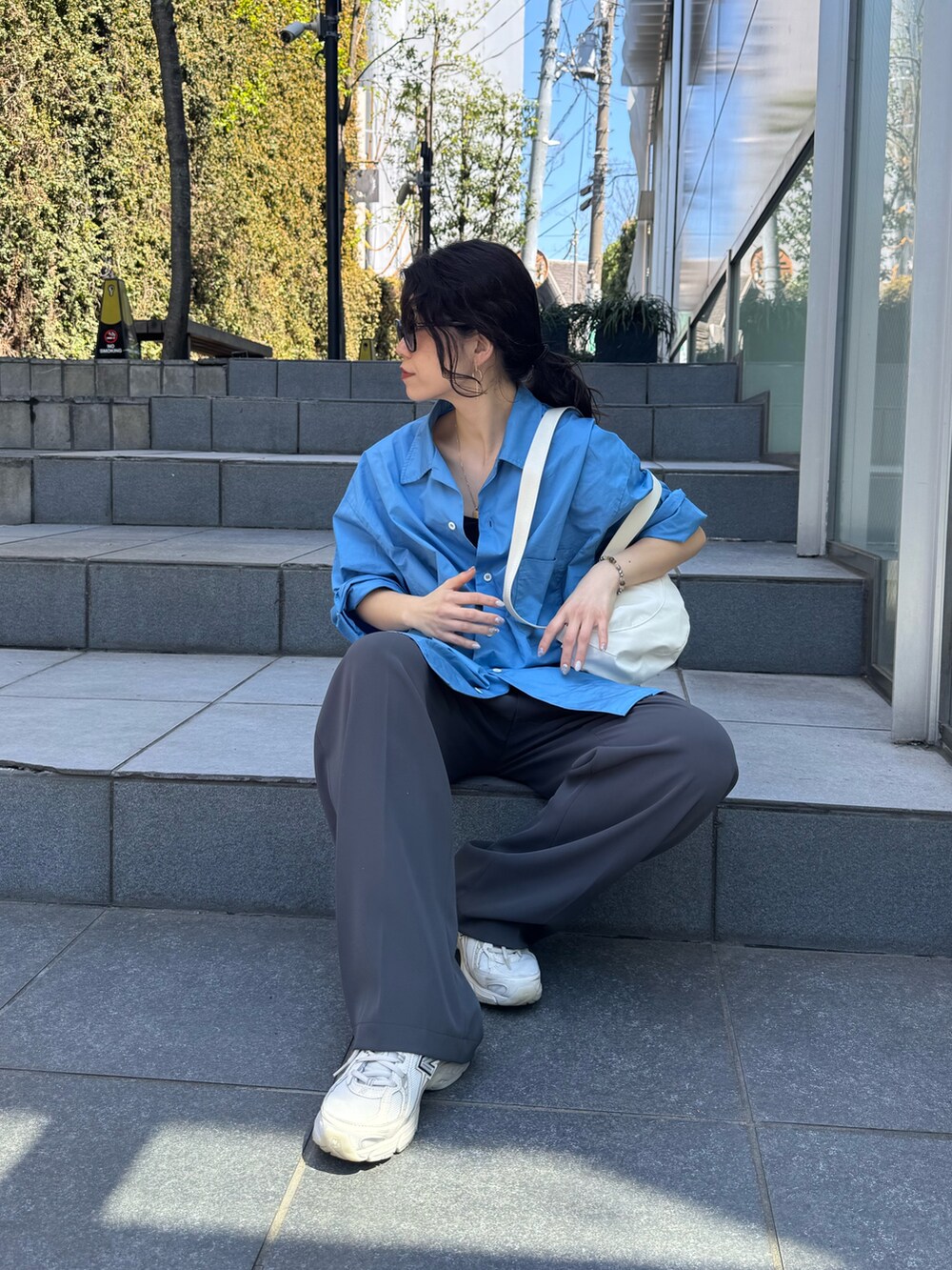 ブルー系のシャツ/ブラウス、グレー系のスラックス、ホワイト系のショルダーバッグを着用したレディースの春コーディネートの4枚目の写真