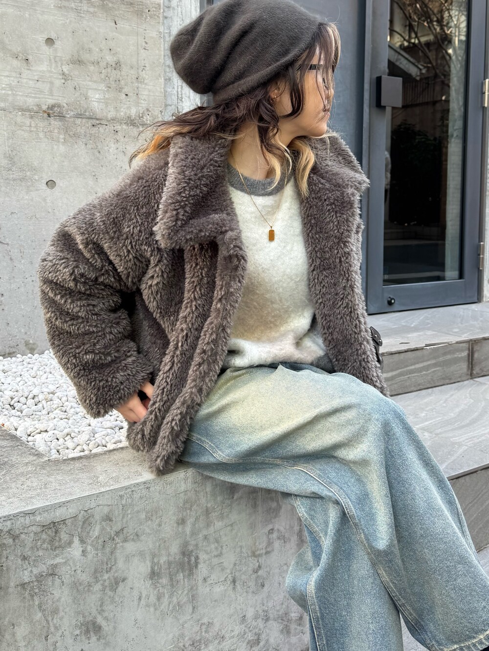 グレー系のムートンコート、ブルー系のデニムパンツ、グレー系のニット/セーターを着用したレディースの冬コーディネートの5枚目の写真