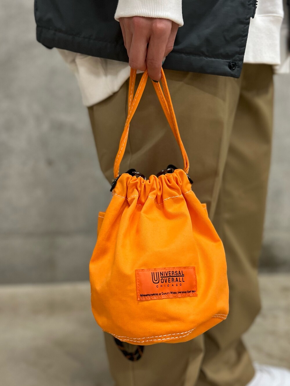 グレー系のベスト、ベージュ系のその他パンツ、オレンジ系のショルダーバッグを着用したレディースの春コーディネートの5枚目の写真