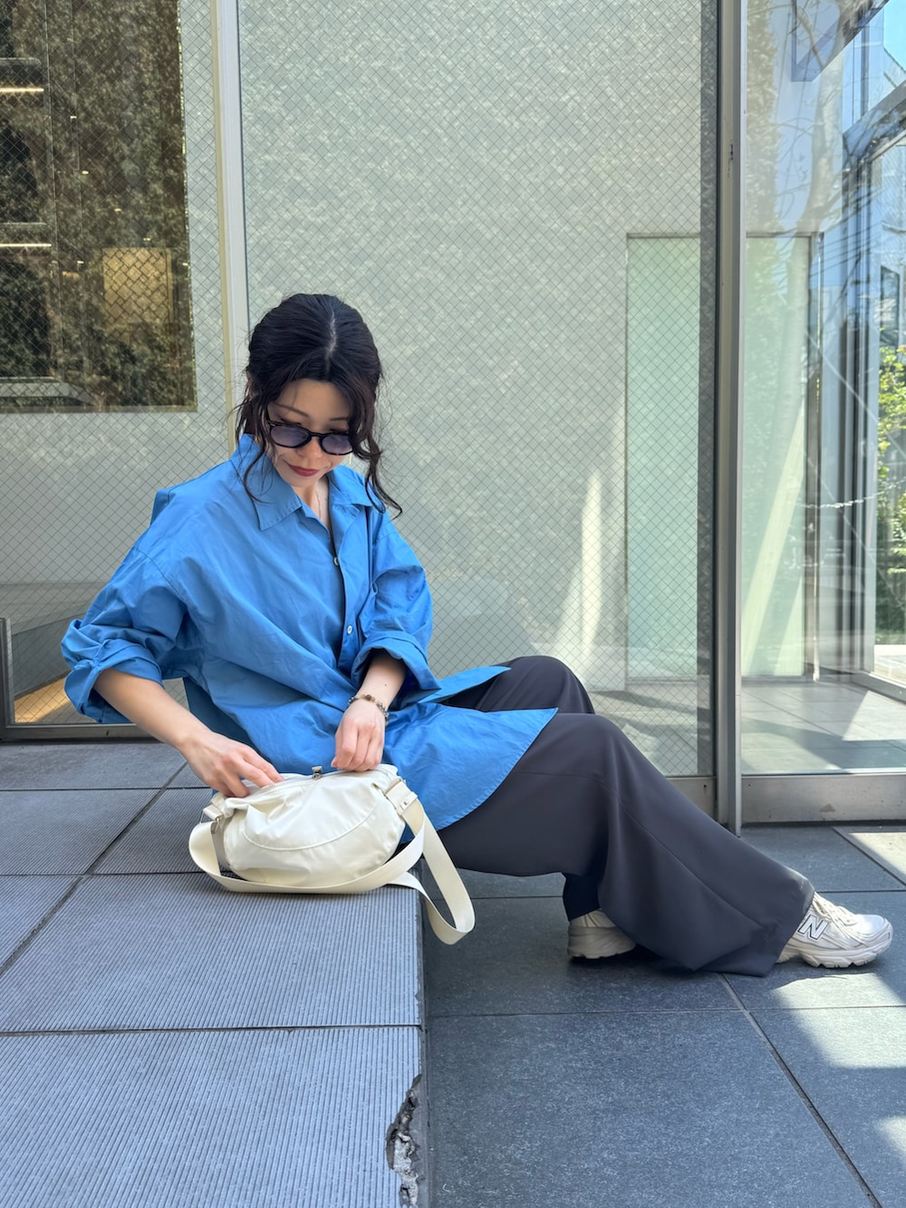 ブルー系のシャツ/ブラウス、グレー系のスラックス、ホワイト系のショルダーバッグを着用したレディースの春コーディネートの2枚目の写真