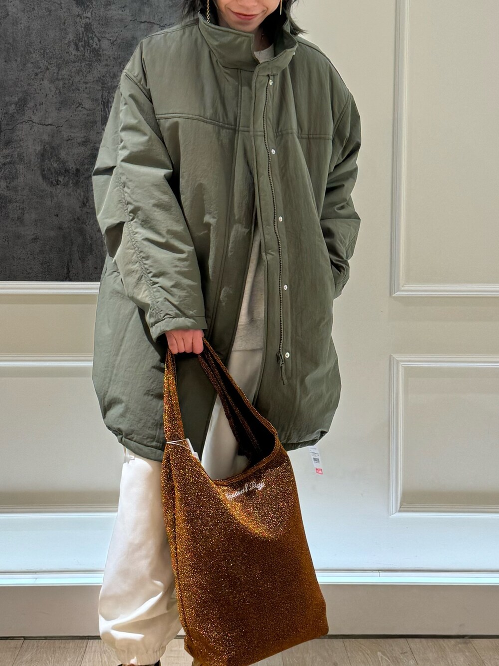 グリーン系のモッズコート、オレンジ系のトートバッグ、ホワイト系のカーゴパンツを着用したレディースの冬コーディネートの2枚目の写真