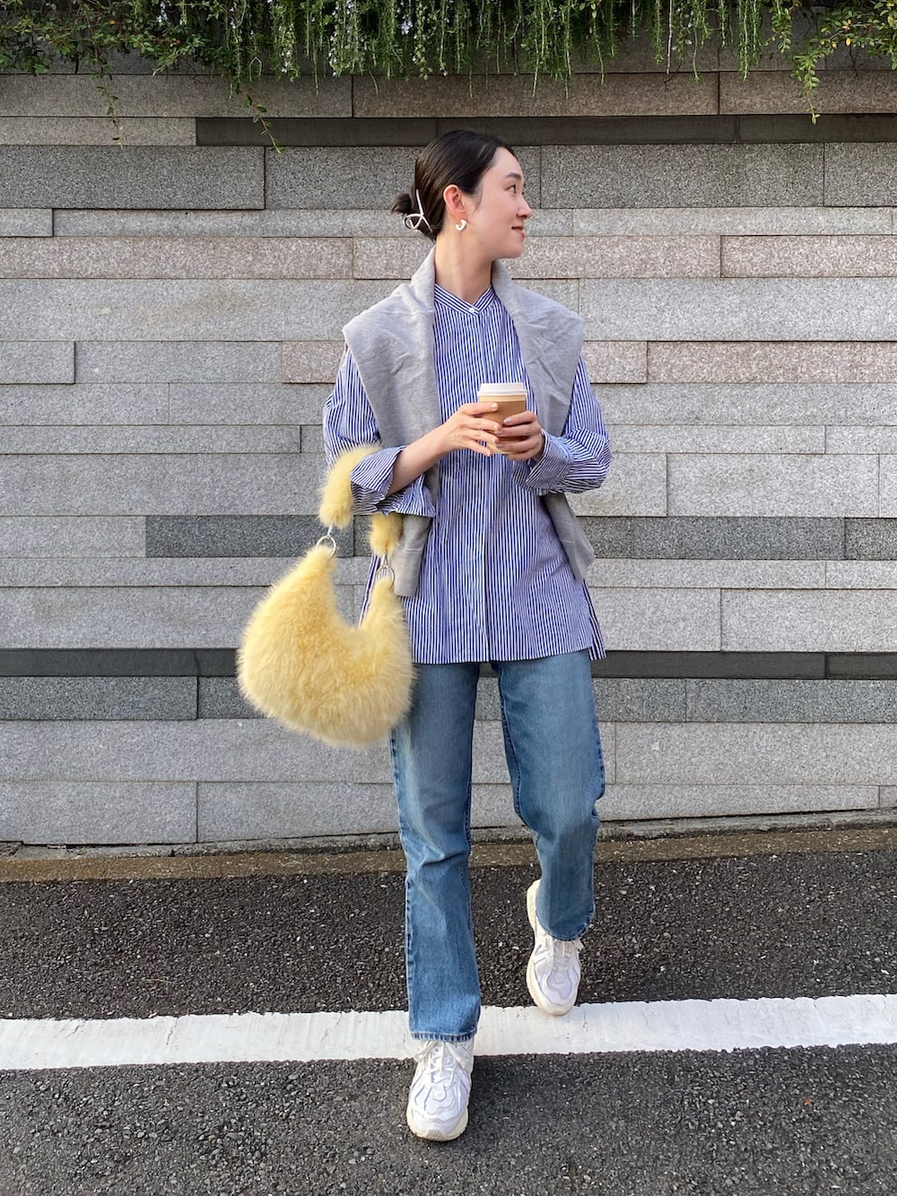 イエロー系のハンドバッグ、ブルー系のデニムパンツ、ホワイト系のスニーカーを着用したレディースの秋コーディネートの3枚目の写真