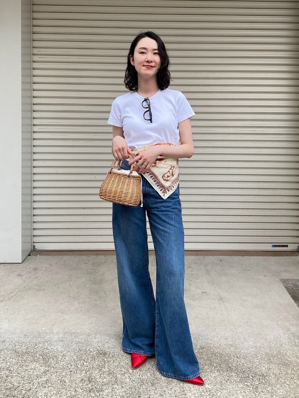 ベージュ系のかごバッグ、ブルー系のデニムパンツ、レッド系のパンプスを着用したレディースの夏コーディネートの2枚目の写真