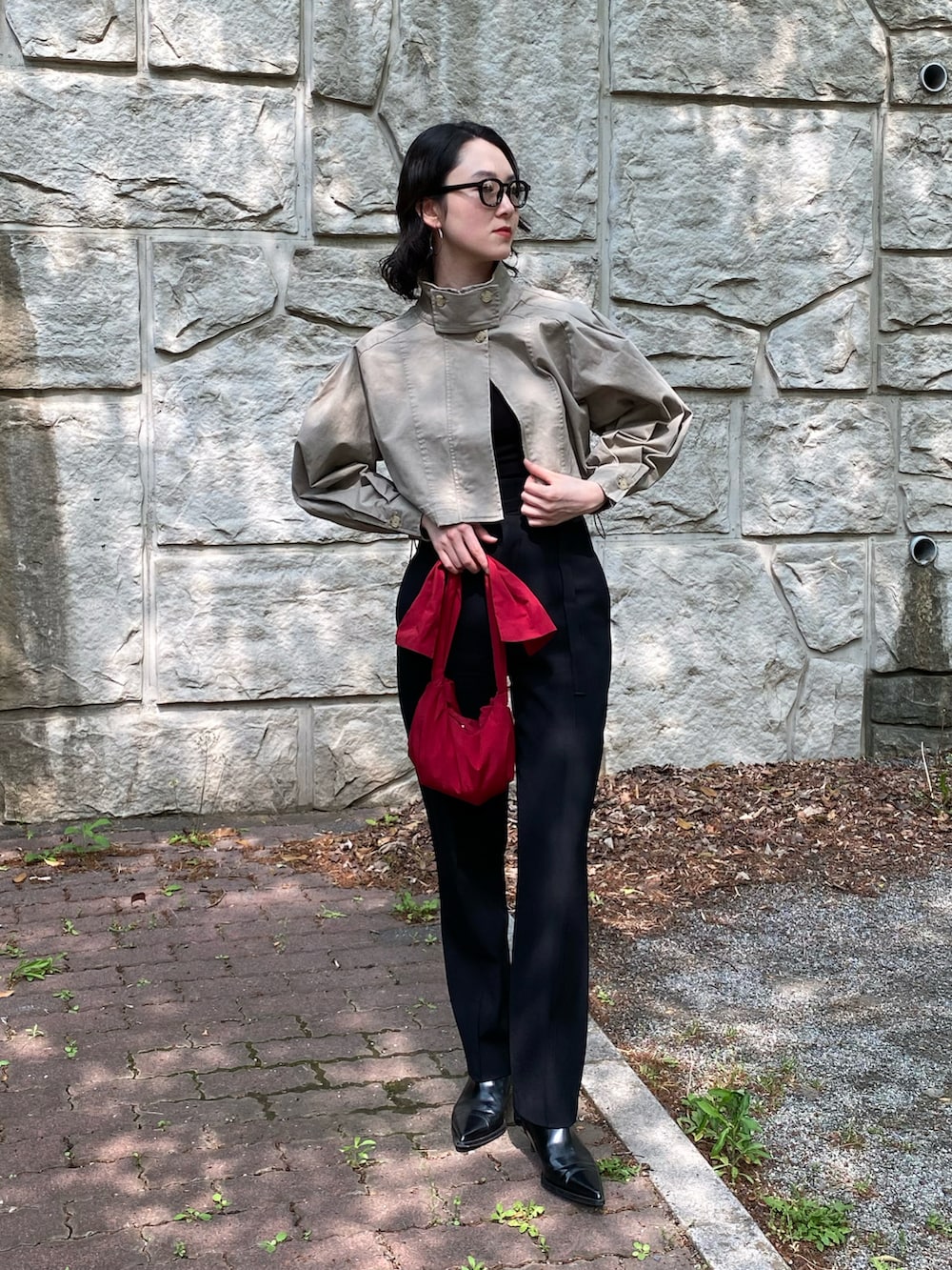 レッド系のハンドバッグ、ベージュ系のミリタリージャケット、ブラック系のパンツを着用したレディースの春コーディネートの3枚目の写真