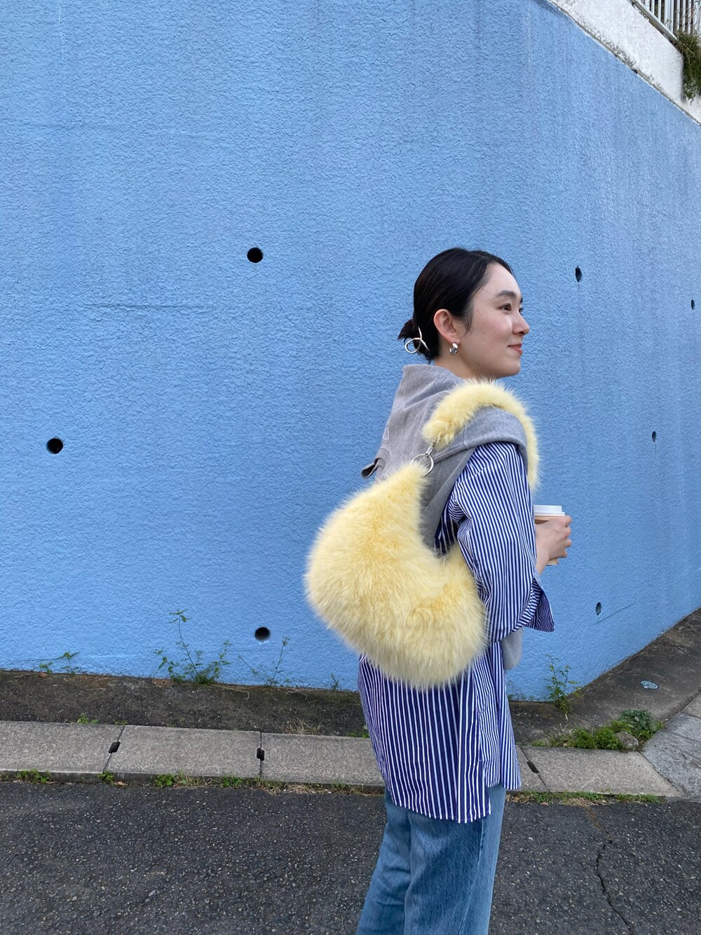 イエロー系のハンドバッグ、ブルー系のデニムパンツ、ホワイト系のスニーカーを着用したレディースの秋コーディネートの2枚目の写真