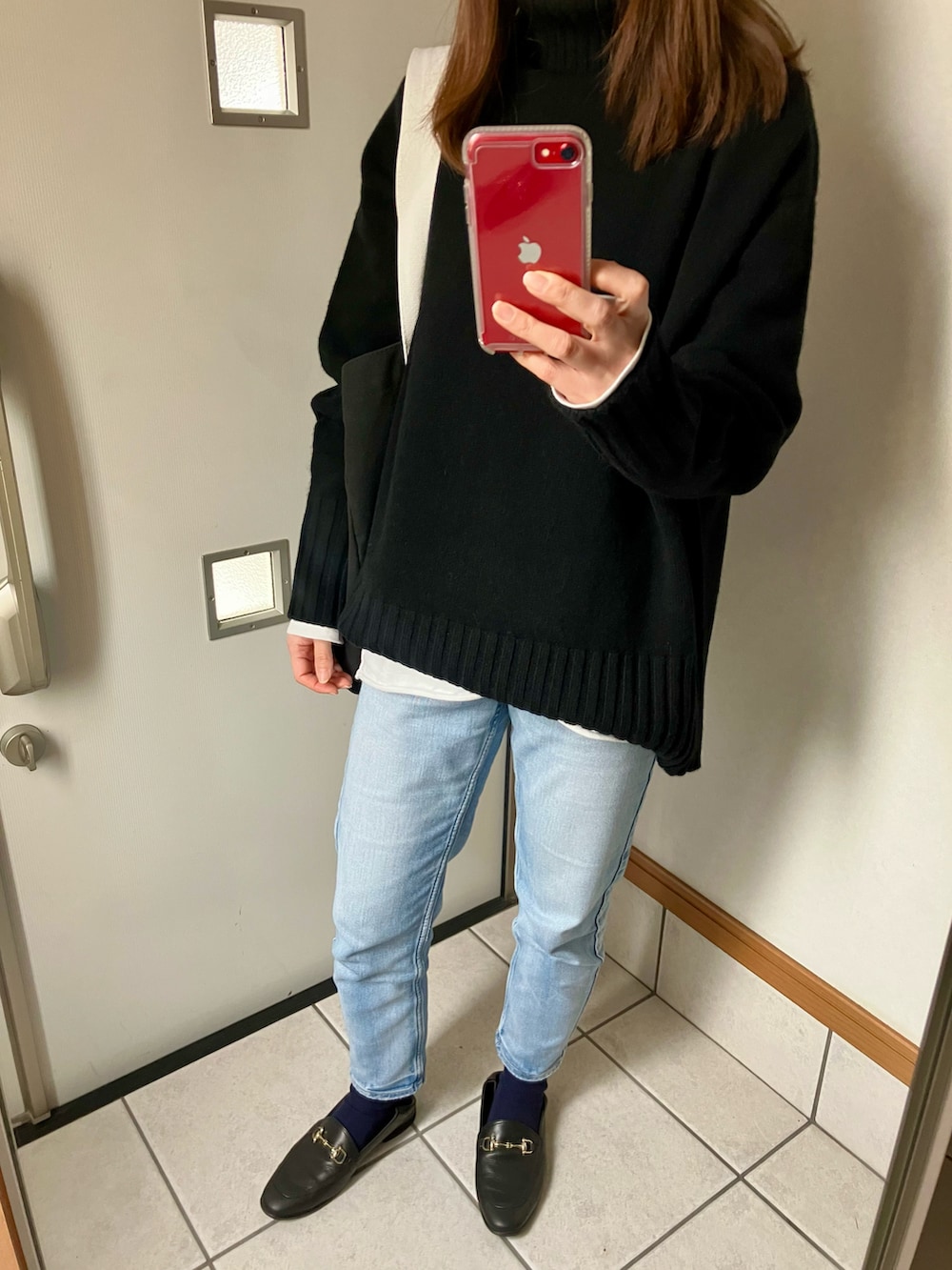 ブラック系のニット/セーター、ホワイト系のTシャツ/カットソー、ブルー系のデニムパンツを着用したレディースの冬コーディネートの2枚目の写真