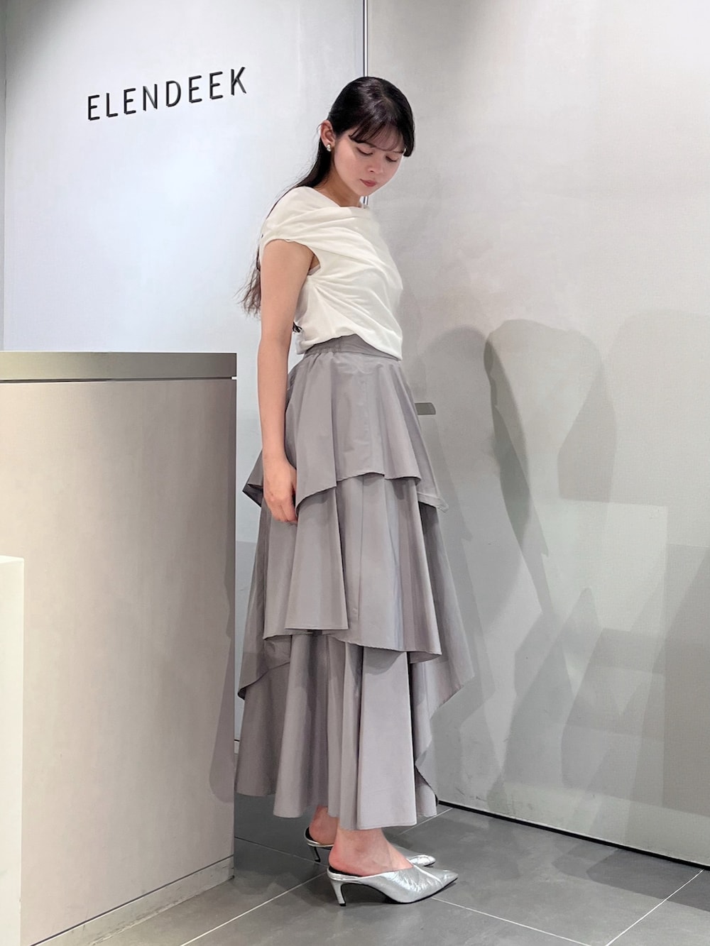 ホワイト系のTシャツ/カットソー、グレー系のスカート、シルバー系のパンプスを着用したレディースの夏コーディネートの2枚目の写真