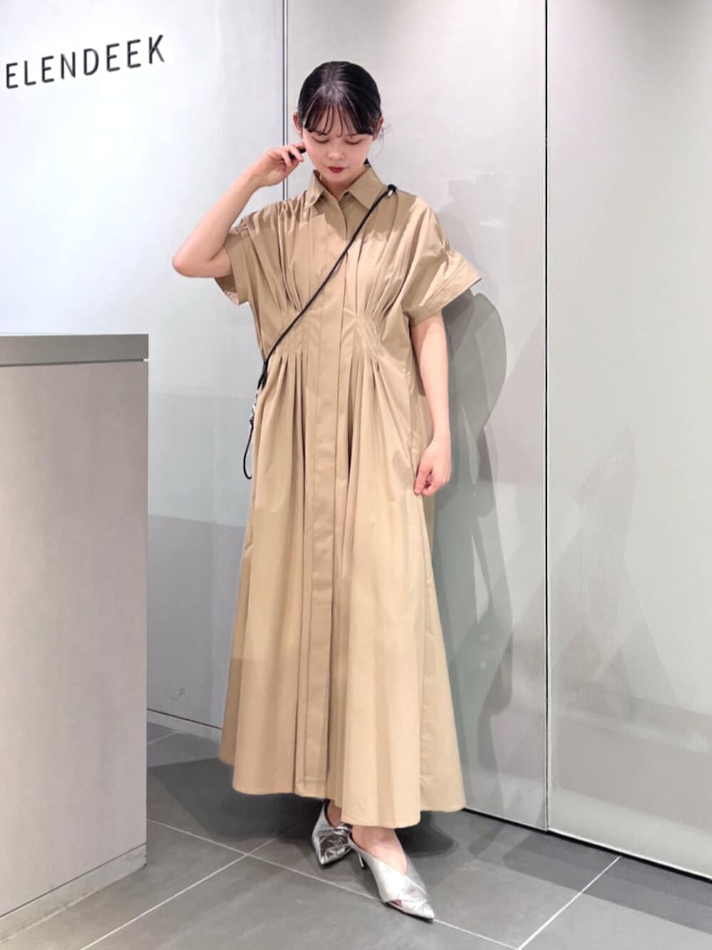 シルバー系のパンプス、ベージュ系のワンピース、ブラック系のスマホグッズを着用したレディースの夏コーディネートの2枚目の写真