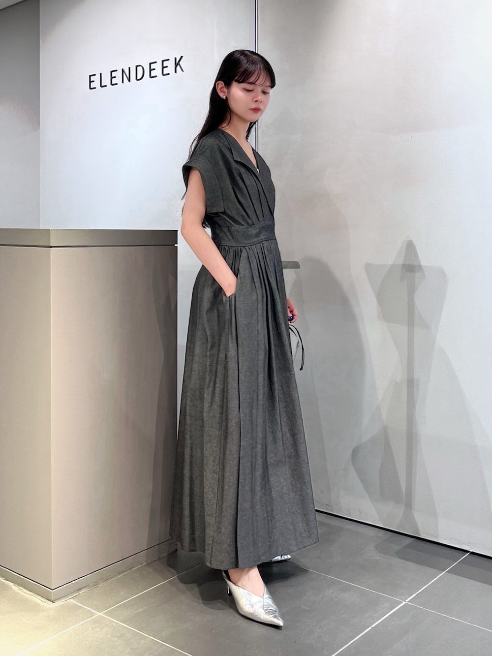 グレー系のワンピース、シルバー系のハンドバッグ、シルバー系のパンプスを着用したレディースの夏コーディネートの2枚目の写真