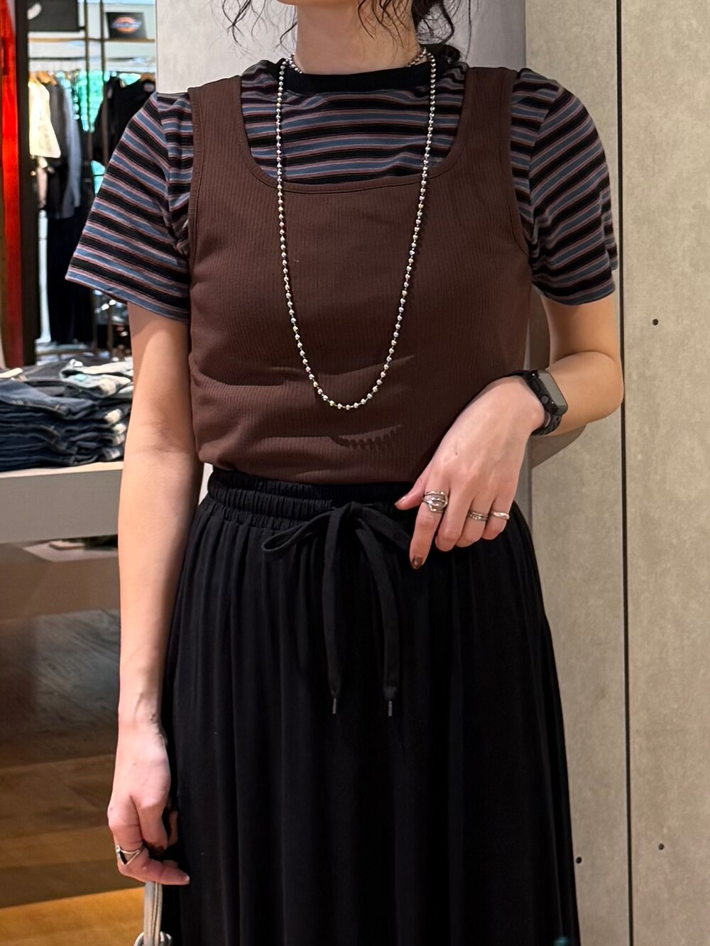 ブラック系のスカート、ブルー系のTシャツ/カットソー、ブラウン系のタンクトップを着用したレディースの夏コーディネートの7枚目の写真