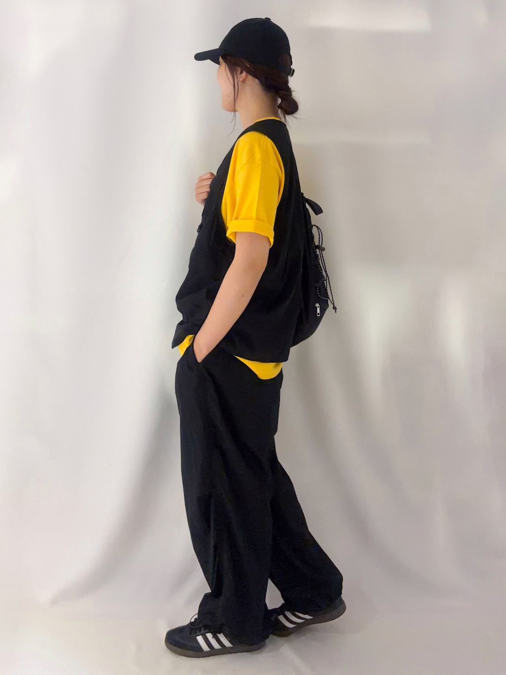 ブラック系のショルダーバッグ、イエロー系のTシャツ/カットソー、ブラック系のキャップを着用したレディースの夏コーディネートの2枚目の写真