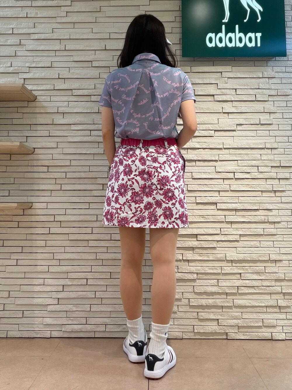 パープル系のポロシャツ、ピンク系のスカート、ブルー系のトートバッグを着用したレディースの夏コーディネートの3枚目の写真